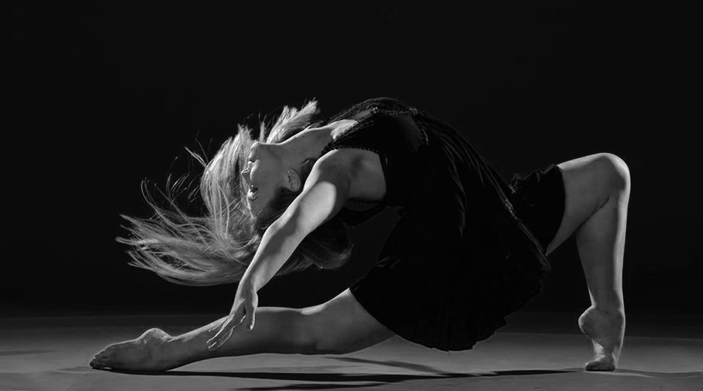 A dancer in a deep backbend, lit against a dark stage.